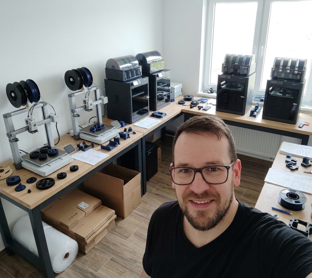 Rafał w swoim warsztacie druku 3D, trzymający wydrukowane zębatki